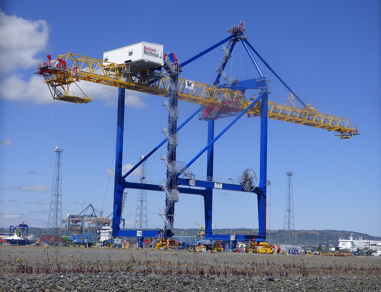 푸른 다리와 노란 붐을 가진 대형 컨테이너 갠트리 크레인이 항만 부두에 설치되어 있고 배경에 선박이 보인다.
